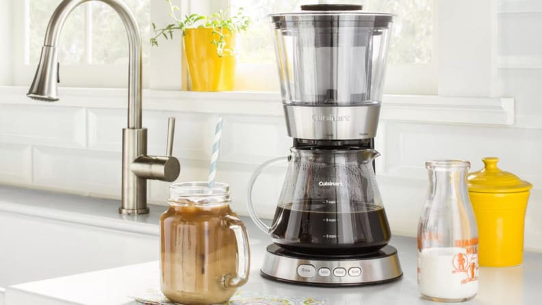 Mason jar of iced coffee next to a coffee maker and glass of milk on kitchen counter