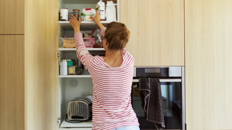 Woman reaching up to top shelf in cabinet.