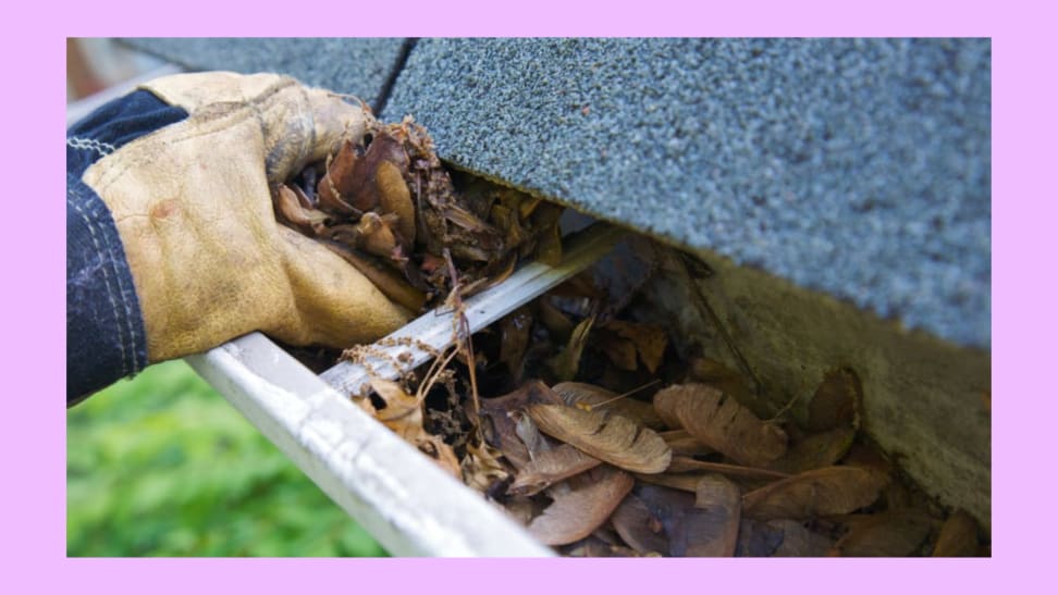 Person wearing work gloves scooping out leaves and debris from gutter