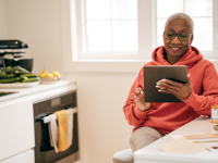 Senior woman smiling at tablet in well lit kitchen.