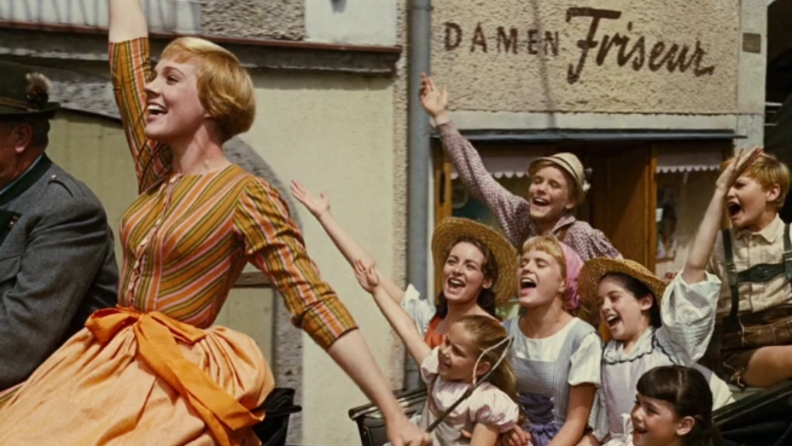 A still from 'The Sound of Music' featuring Maria in a cart singing with the von Trapp children.