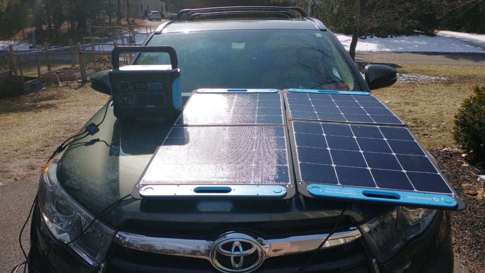 Person using small generator and solar powered panel on top of hood of car.