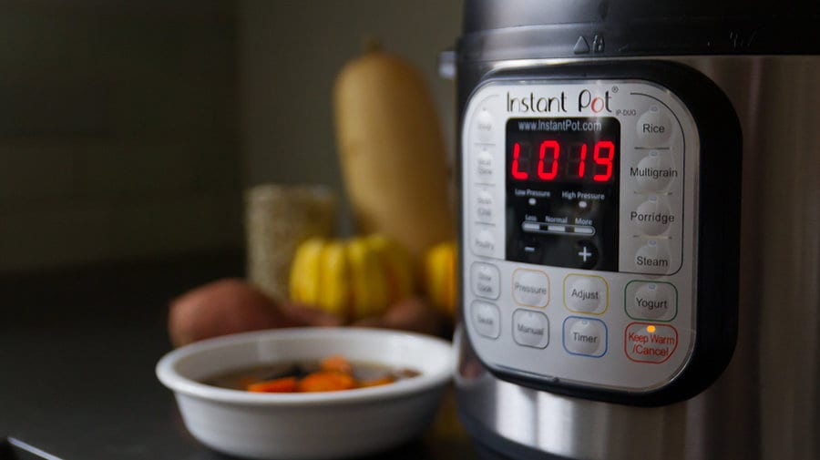 A close up of the control panel of an Instant Pot with a bowl of soup and some fall vegetables in the background.