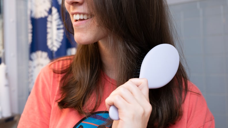 A person brushing through their brown hair with one of the best hair brushes.