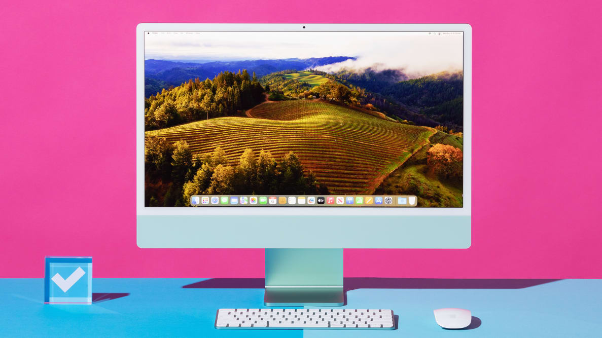 An all-in-one iMac desktop computer standing on a blue surface against a hot pink background