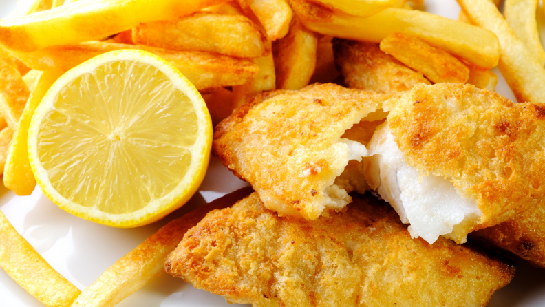 A plate of fried fish with french fries and a fresh lemon wedge.