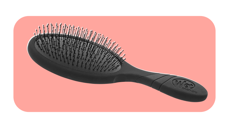 A black hair brush on a pink background.