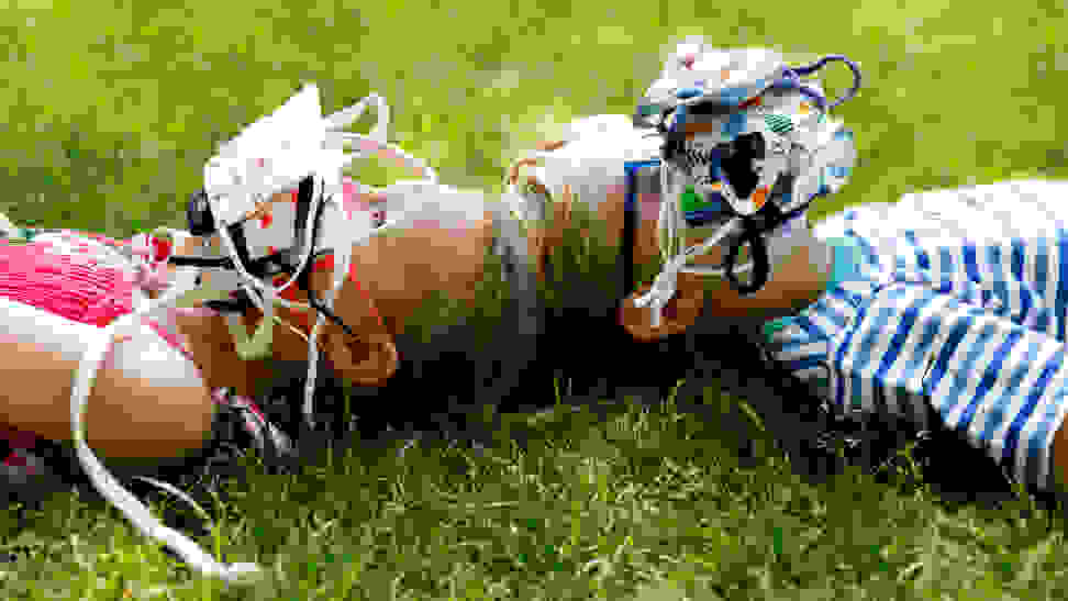 Two young children laying on the grass with their faces covered in a piles of face masks