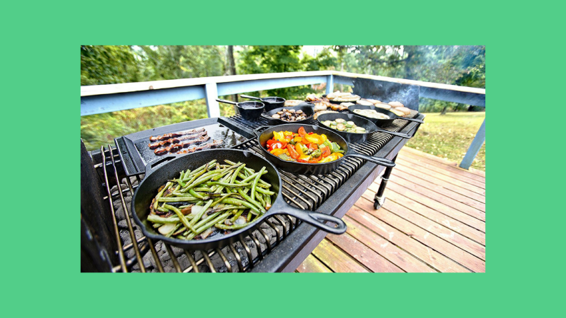 Cast iron skillets full of vegetables lined up on a large grill outdoors.