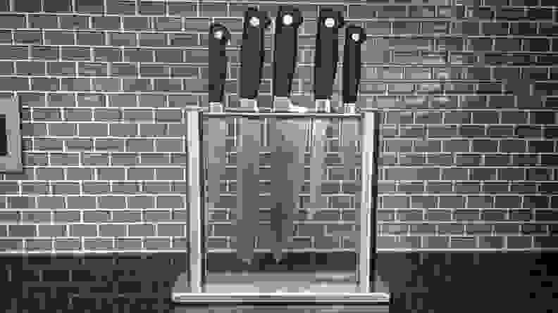 A 5-piece knife sett in a thin glass case against  a subway tile kitchen backsplash.