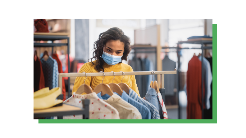 A person in a yellow shirt and mask looks through a rack of shirts.