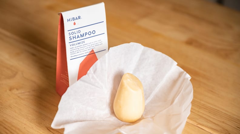 The HiBar Volumize Shampoo Bar cardboard box with the shampoo bar sitting in front of it inside a paper casing.