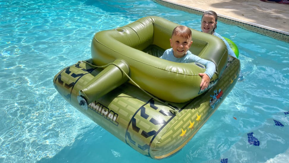 Two children smiling inside of tank-shaped pool inflatable outdoors in pool.