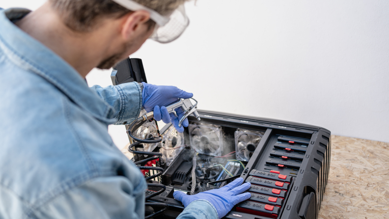 A person with clear goggles on dusting electronic equipment