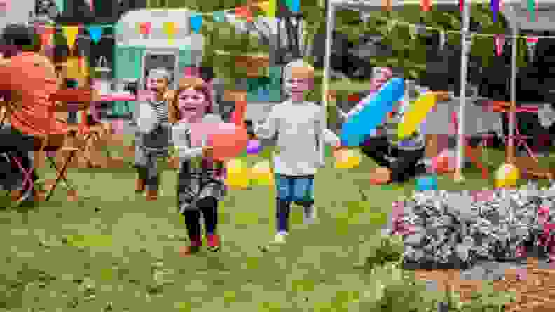 Kids running through a yard with balloons while at a party.