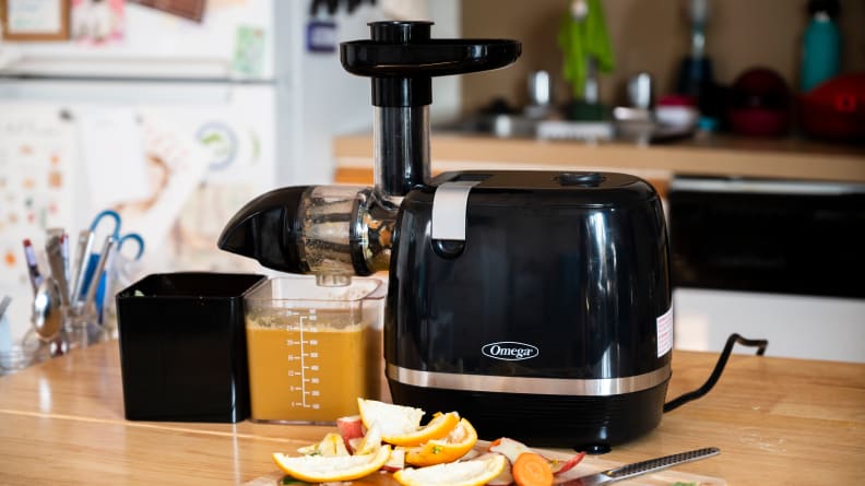 Omega H3000D Cold Press 365 Juicer sits on a counter in a kitchen with citrus peels in front of it and a full cup of orange juice.