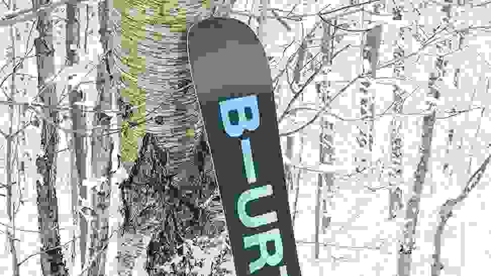 A burton snowboard leaning on a tree next to a ski trail.