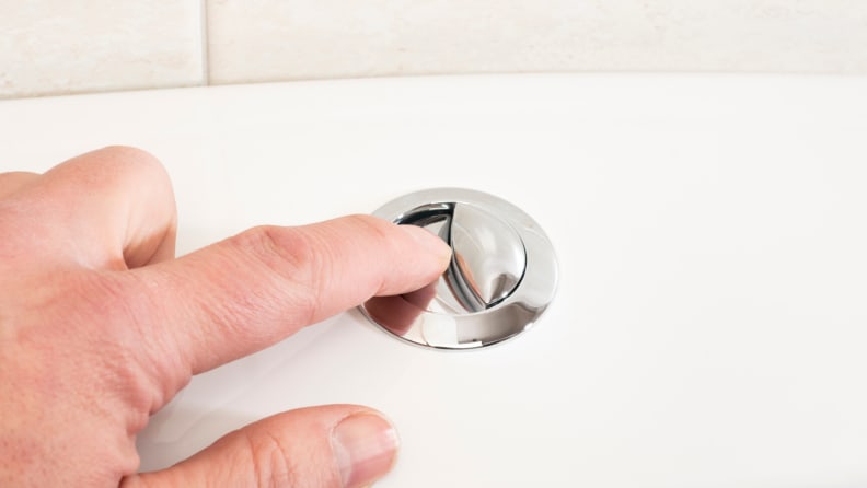 Person pressing silver button on the top of dual flush toilet