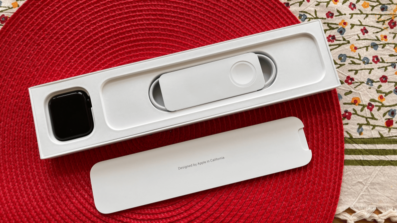 Apple Watch SE shown inside the box on a red mat.