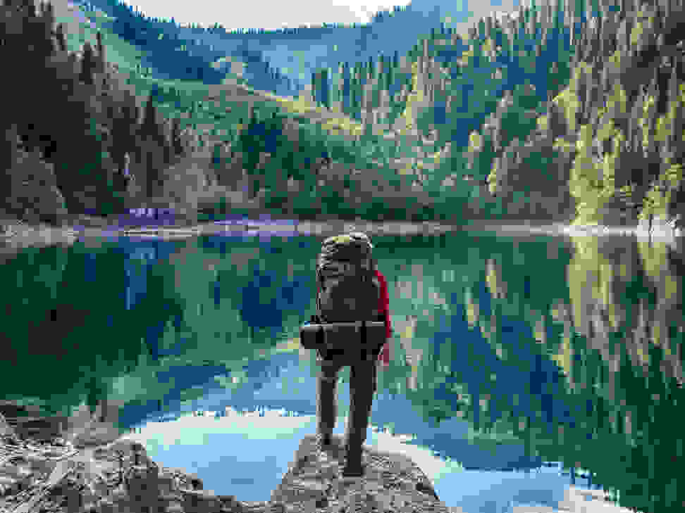 A hiker overlooks a beautiful body of water surrounded by hills and trees.