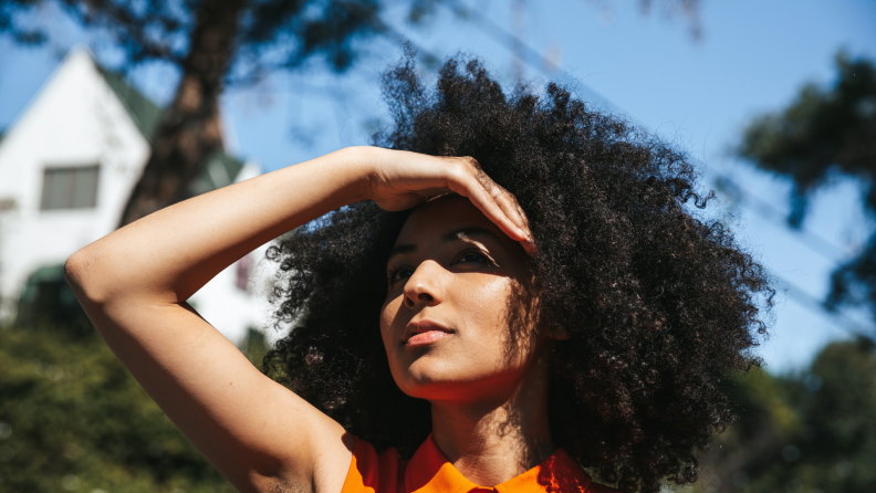 A woman standing in the sun with her hand over her eyes blocking the sun