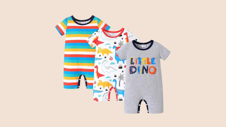 Three rompers stacked one on top of the other. In the back is a striped romper in blue, teal, yellow, white, and red-orange; in the middle, a romper with a dinosaur pattern; in the front, a romper with the graphic letters "Little Dino."