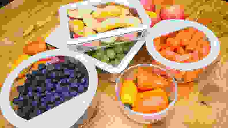 Assorted fruits and vegetables sit inside of separate food storage containers on top of wooden surface.