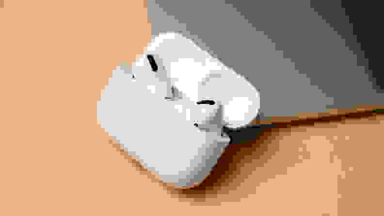白色无线耳机放在米色的桌子上，旁边放着一台笔记本电脑。