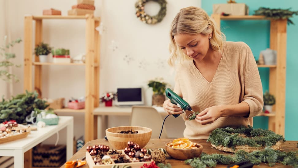 Woman using a hot glue gun to attach dried fruit to an evergreen Christmas wreath