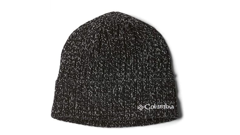 Displayed against a white backdrop, a knit black Columbia hat has bits of white in it, creating an ashy pattern like television static.