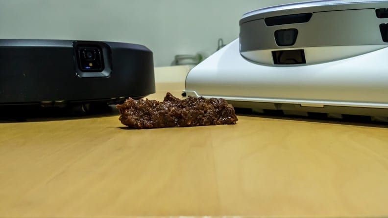 The iRobot Roomba j7+ and Samsung JetBot A.I.+ sit on a table with fake pet poop in front of them