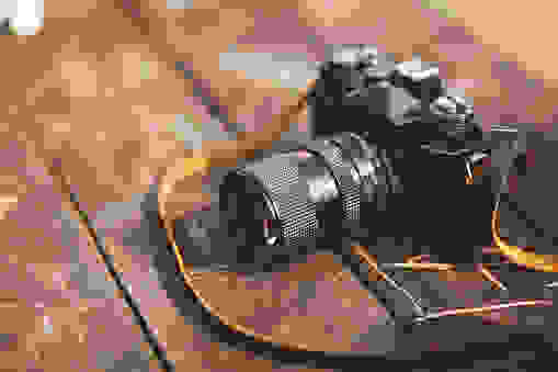 vintage toned image of an old film camera, lying on the wooden table. shot with faded cross processing technique.
