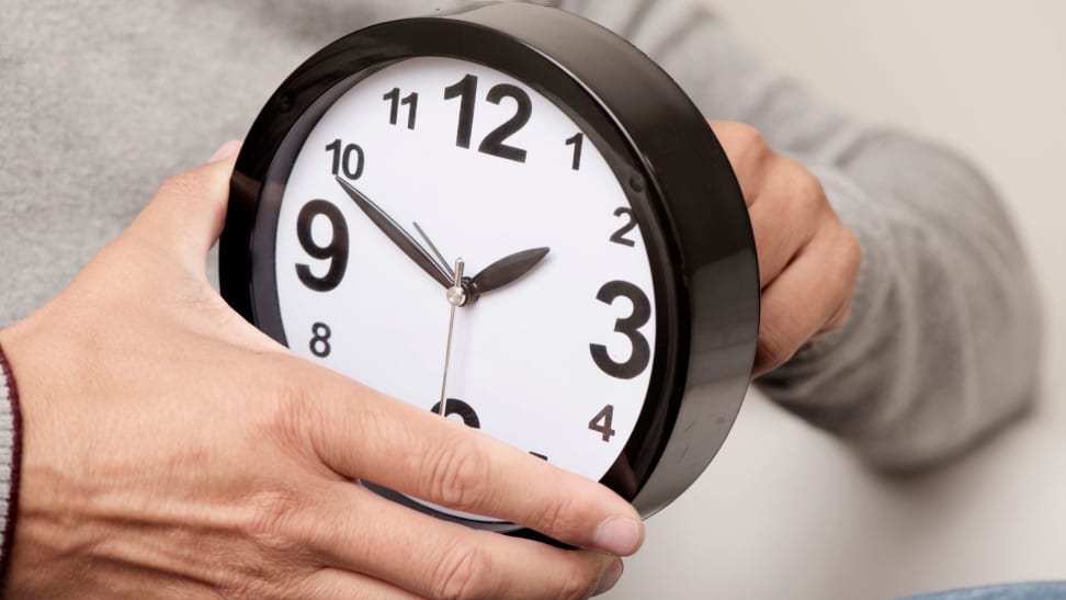 a man holds a clock and changes the time on it.