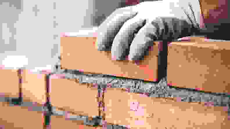 A person's hand holding a brick while it is being put together with other bricks with mortar.