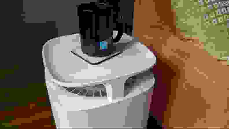A coffee cup sits on top of an air purifier in a living room.