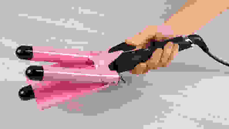 A hand holding out a pink and black hair waver and pulling the clamp back to open it.