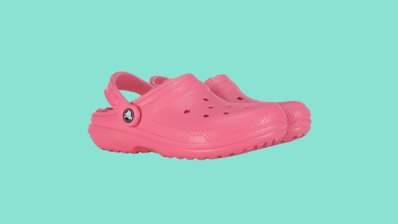 Side view of a pair of pink fuzz-lined Crocs on a dark teal background.