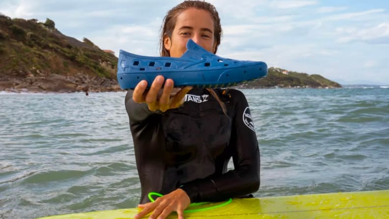 Woman holding single Vans Trek Slip-On shoe on a surferboard