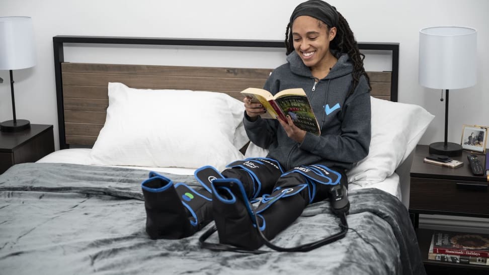 Woman sitting and bed reading a book with a compression massager on her legs.