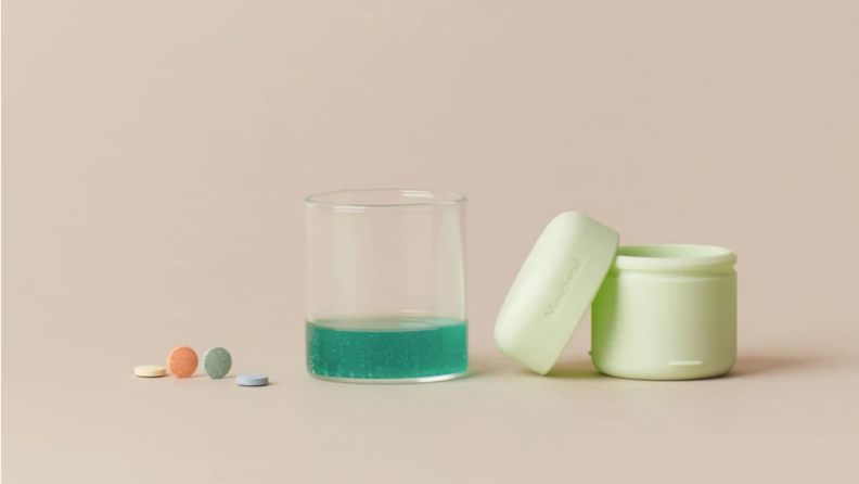 Mouthwash tablets, a carrying case, and mouthwash in a glass.