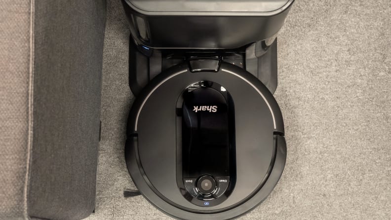 A circular black Shark IQ robot vacuum trundles along on the carpet. We're looking down at it from above.