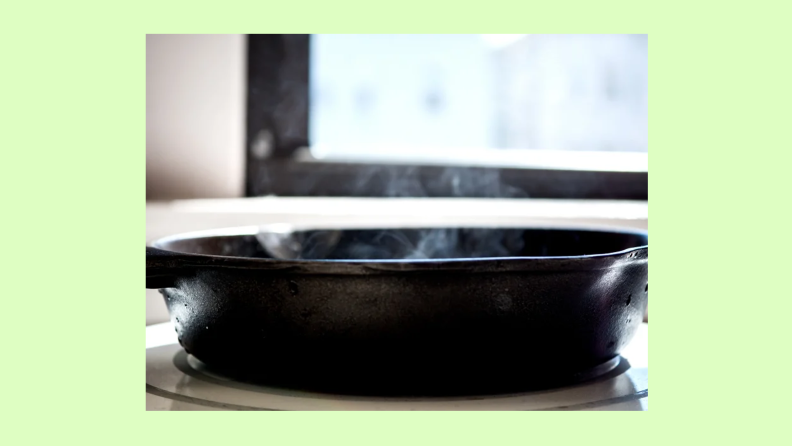 A cast-iron pan sits on a burner and smoke rises from the pan.