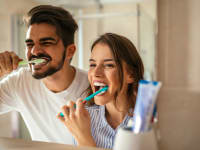 A photo of a man and woman brushing their teeth together.
