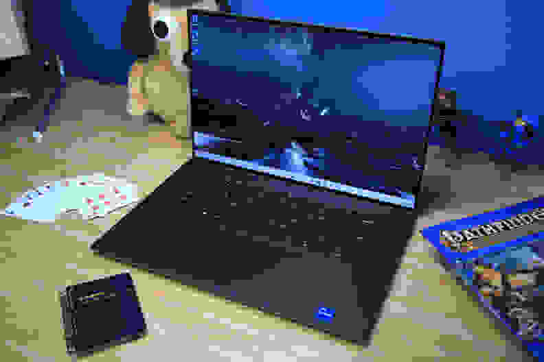 A laptop open and powered on flanked by knickknacks on top of a light brown wooden surface