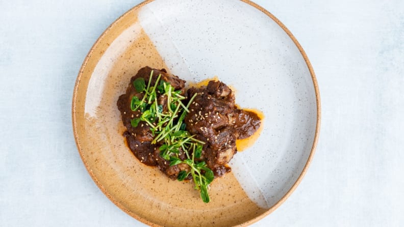 A top-down photo of a plate filled with braised oxtail topped with micro greens.
