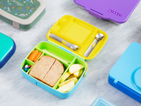 Bento boxes, cheese stick, carrots, apple, a sandwich, and M&Ms in a lunchbox, laid out on a marble counter.