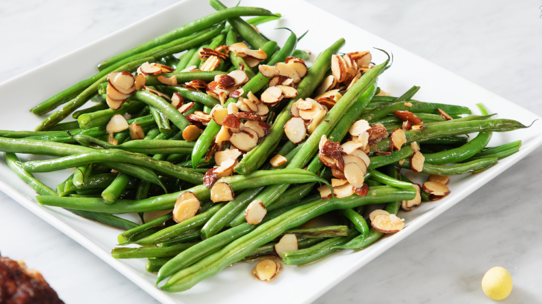 Green beans topped with sliced almonds served on a white plate.