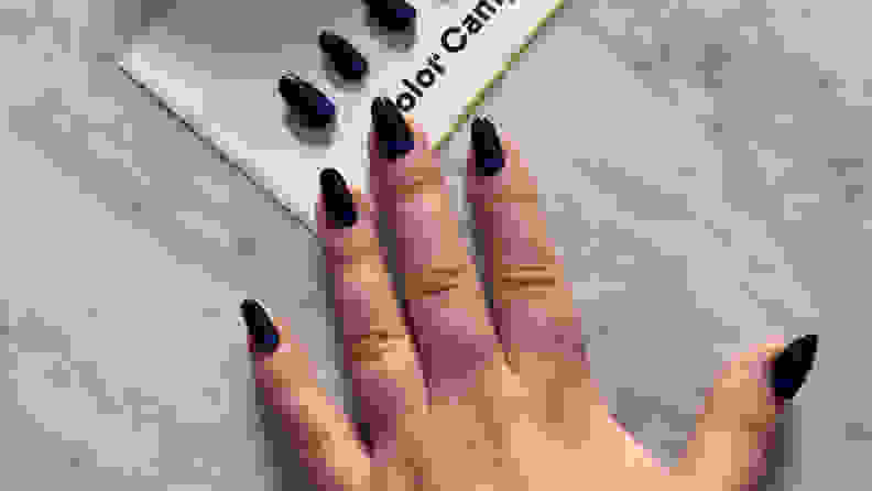 A hand wearing press-on nails laying on a marble tabletop in front of a set of matching press-ons.