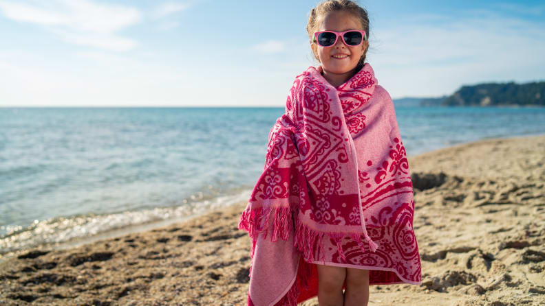 A little girl wrapped in a pink beach towel standing on the beach