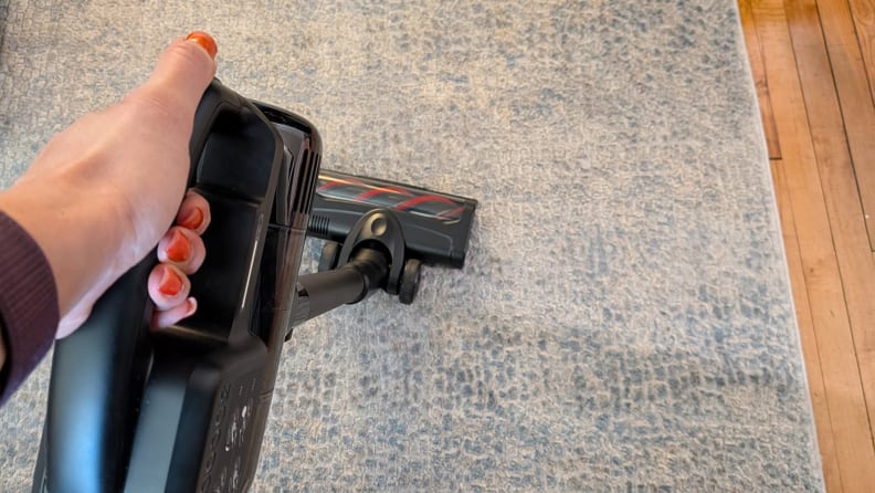 A hand holding a stick vacuum on a carpet